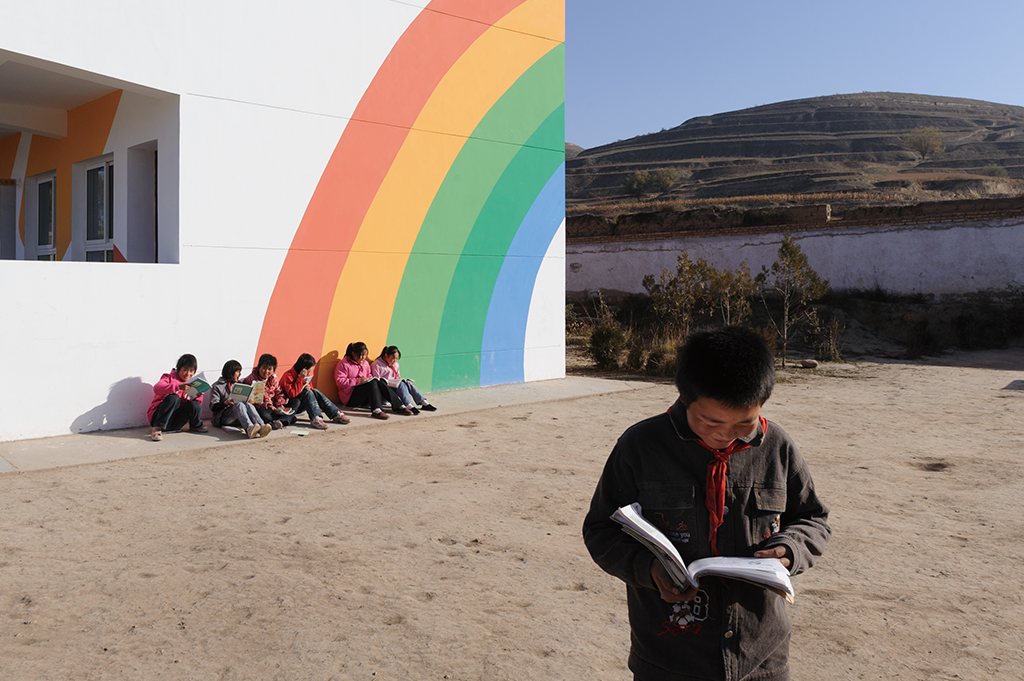A school wall painted with a rainbow, and a pupil reading outdoors