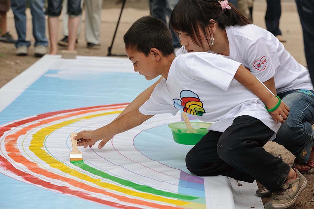 Children painting a rainbow on the ground with brushes