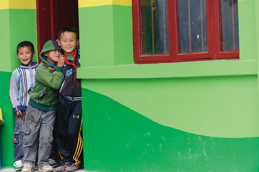 Three children standing beside a freshly painted green school building