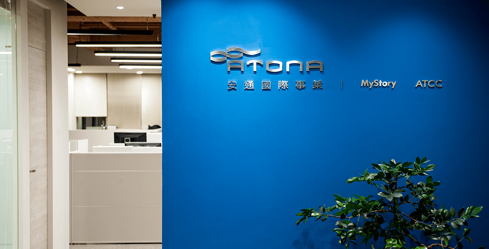 安通國際辦公室接待區，藍色牆面上有 ATONA、MyStory 與 ATCC 識別
